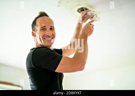 Handsome young builder installing light on the ceiling Stock Photo