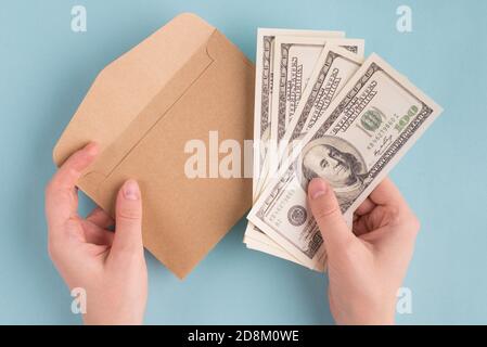 First person above top overhead view photo of female woman hands holding stack pile of american dollars and craft paper envelope isolated over blue co Stock Photo