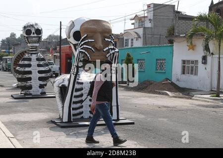 Mexico City, Mexico. 30th Oct, 2020. MEXICO CITY, MEXICO - OCTOBER 30: A person wears face mask while walks front a monumental skull made of cardboard, were put to decorate the streets Of Tlahuac to celebrate Day of the Dead ( Dia de Muertos) amid Covid-19 pandemic. on October 30, 2020 in Mexico City, Mexico. Credit: Ismael Rosas/Eyepix Group/The Photo Access Credit: The Photo Access/Alamy Live News Stock Photo