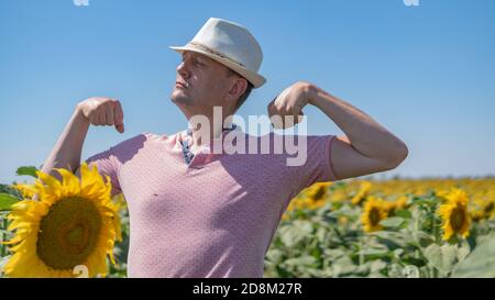 In a field with sunflowers a handsome guy on a blue background in a hat Stock Photo