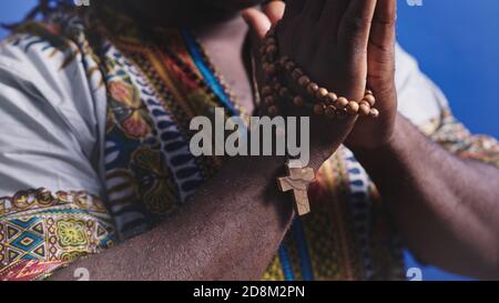 Unrecognizable African black man in traditional dress with rosary praying with hands over his chests. High quality photo Stock Photo