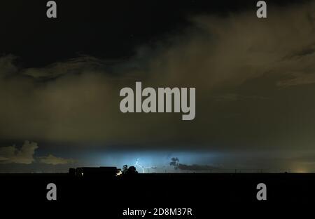 Thundercloud with lightning bolt hitting the earth behind a farm in the dutch countryside Stock Photo