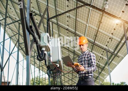 Male engineer working with laptop and sensor, on the background of the solar power station. Solar panels, sunny power electricity. Innovation future. Modern technology. Stock Photo