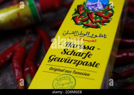 Viersen, Germany - October 9. 2020: View on yellow packet tunisian harissa spice paste tube with red chillies background Stock Photo