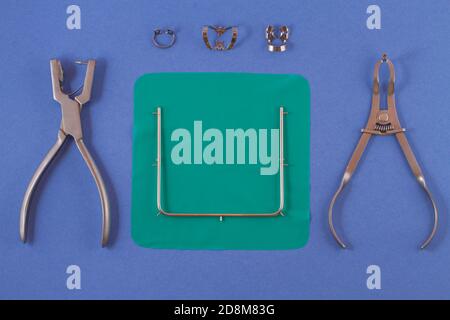 Tools for installing the cofferdam. Rubberdam and clamp lying on the table a blue background. Stock Photo