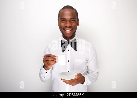 Portrait of happy young black man in bowtie holding cup of coffee against white background Stock Photo