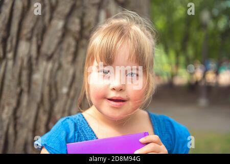 A portrait of trisomie 21 child girl outside having fun on a park reading book Stock Photo