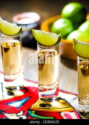 Three shots of tequila in tall shot glasses with lime wedges on top Stock Photo