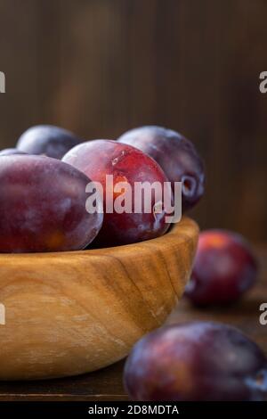 Fresh plums in a wooden bowl on a brown table. Gathering the summer harvest. Stock Photo