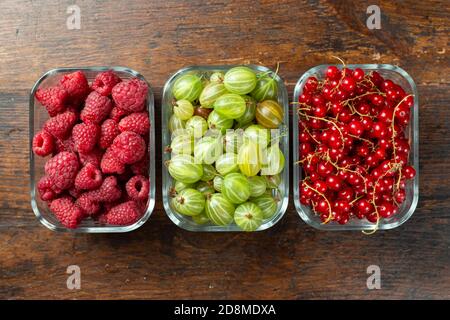 Assorted berries of raspberries, gooseberries and red currants in glass bowls on a wooden table. Stock Photo