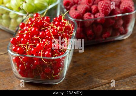 Assorted berries of raspberries, gooseberries and red currants in glass bowls on a wooden table. Stock Photo