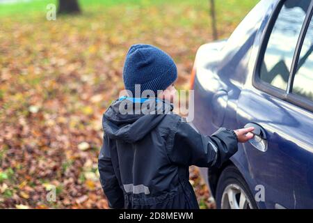 A little boy walking in the Park on an autumn day. Goes to the car and opens the car door. Stock Photo