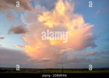 Dramatic stormy sunset over rural area with puffy clouds lit by orange setting sun and blue sky. Stock Photo