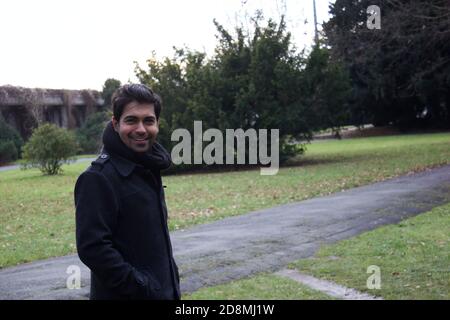 An asian ethnicity Indian man smiling in a coat and scarf during winters in a park / outdoor Stock Photo