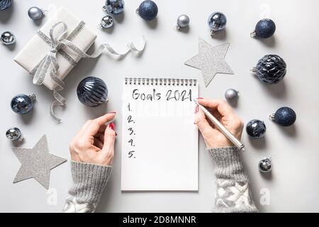 Woman writes goals for New 2021 Year, checklist, plans and dreams on blue Holiday background with gift. Top view. Flat lay. Stock Photo