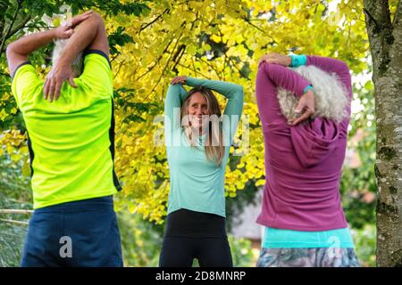 A couple in their sixties exercise with a young female personal trainer outdoors. Stock Photo