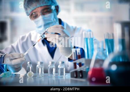 Virologist filling a syringe researching vaccine in laboratory bench. Horizontal composition. Front view. Stock Photo