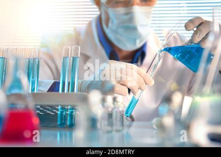 Scientist pouring blue liquid from a beaker into a test tube close up. Horizontal composition. Front view. Stock Photo