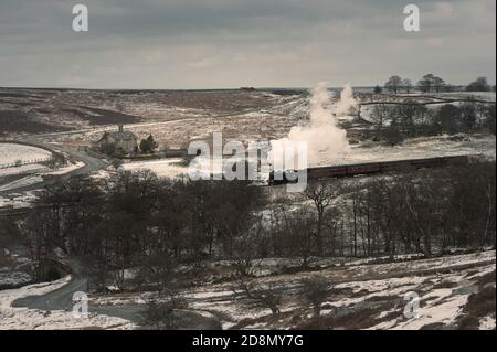 Steam train ploughs through snow-laden rural landscape in heart of the North York Moors in winter near Goathland, Yorkshire, UK. Stock Photo