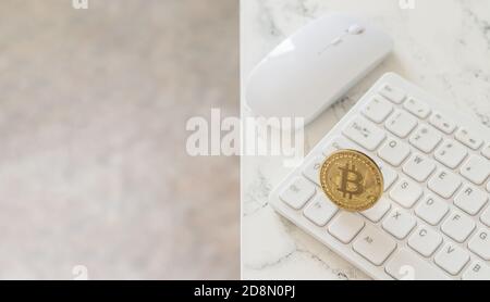 Cryptocurrency gold bitcoin on white computer keyboard next to mouse on marble table Stock Photo