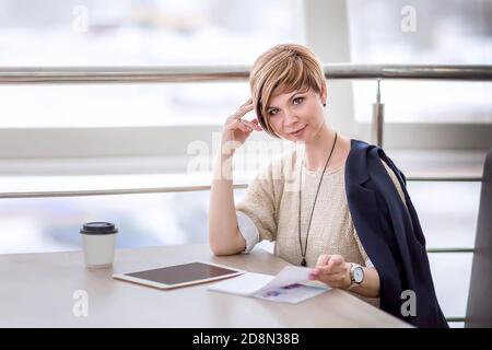 A young beautiful woman is sitting in a cafe, drinking coffee and browsing social media on a tablet. Lifestyle. Portrait of a woman watching social ne Stock Photo