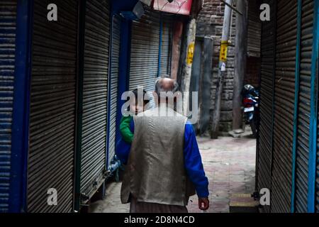 A man carrying a kid walks past closed shops during the shutdown in Kashmir.A shutdown was observed across the Kashmir valley to protest against India's new laws that allow Indians to buy land in the region. The shutdown call was made by a separatist group headed by Mirwaiz Umar Farooq. Stock Photo