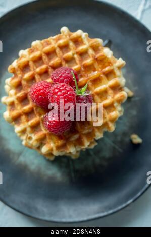 sweet Viennese waffles with fresh ripe raspberries are served for Breakfast on a beautiful plate. top view. Copy space Stock Photo