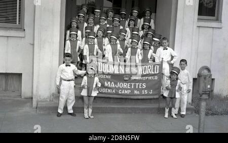 1950s, historical, a group of young children standing at entrance to a building, with two boys holding a a banner saying Woodmen of the World, Majorettes, Eugenia Camp, Springfield, Oregon, USA. Majorettes are children who are associated with marching bands at parades and for baton twirling. The banner has the name of their sponsor, Woodmen of the World Life Insurance Society, a not-for-profit fraternal benefit society founded in the USA in 1890. Stock Photo