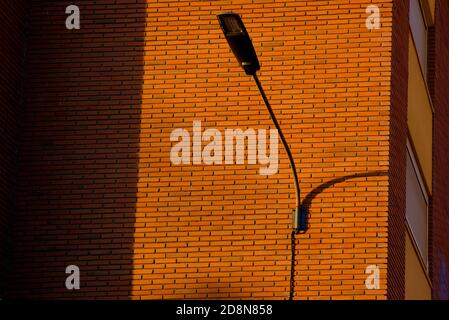 A deep red brick wall supports a lamppost, contrasting and bright colors. Stock Photo