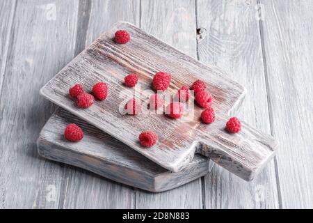 Raspberry fruits on old cutting board, healthy pile of summer berries on grey wooden background, angle view Stock Photo