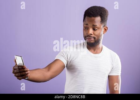 Photo of amazed puzzled black man holding modern cell phone, taking selfie. Reaction, technology, facial expressions concept. Stock Photo