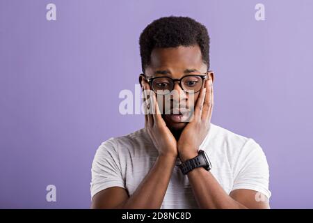 Portrait of surprised astonished african man in glasses wearing white tshirt touching his face with palms and open mouth, being in shock, isolated on Stock Photo