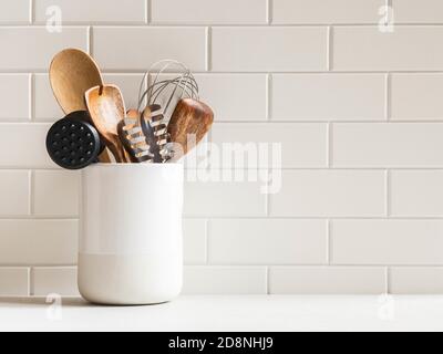Stylish white kitchen background with kitchen utensils in ceramic jar on white countertop, copy space for text, front view Stock Photo