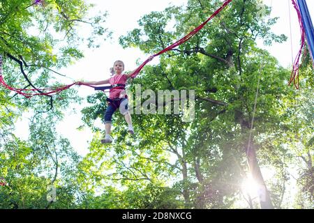 Child girl having fun jumping on trampoline with elastic ropes Stock Photo