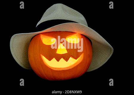 Carved halloween pumpkin wearing a straw hat isolated on a black background Stock Photo