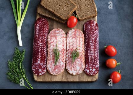 Serving of the slices of smoked sausage of two kinds, salchichon and braunschweig sausages lie on a cutting board in several rows. Nearby are cherry t Stock Photo