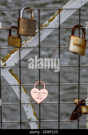 padlocks chained to a fence and some railings on a bridge over the river in leamington spa park uk, keepsakes and mementos from lovers on a fence. Stock Photo