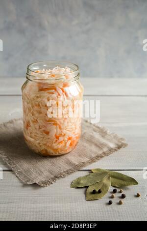 Open glass jar of sauerkraut stands on a canvas napkin. Next to the bay leaf and peppers. Close up composition on a white, wooden background. Fermente Stock Photo