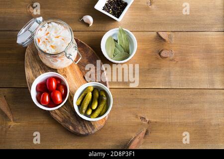 Homemade sauerkraut in glass jar on wooden background. On the stand are bowls with marinated cucumbers and tomatoes. Fermented and pickled food. Close Stock Photo