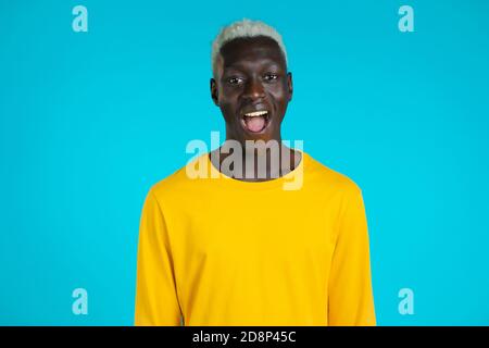 African man depicts amazement, shows WOW delight face effect. Surprised excited happy guy. Handsome male shocked model on blue background. Stock Photo
