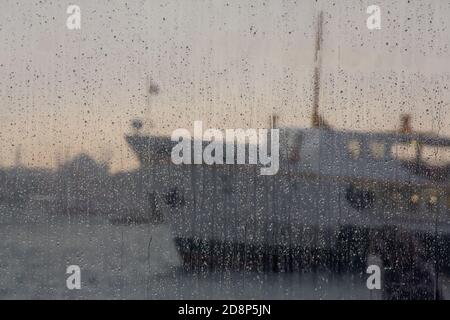 Selective focus shot of a wet window with a view of a big ship on a rainy day Stock Photo