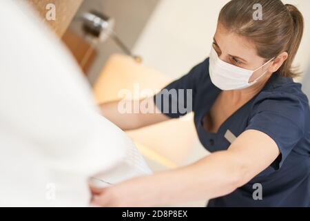 Close up of Caucasian chambermaid in mask adjusting pillows on the bed in hotel room. Hotel service concept Stock Photo