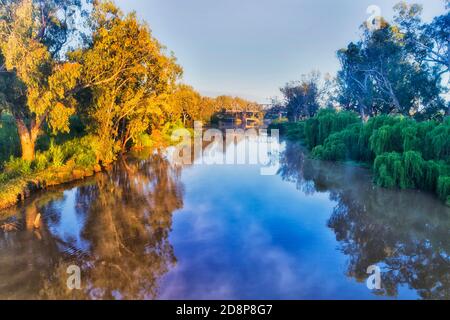 Still calm Macquarie river at sunrise near historic railway bridge in Dubbo city of Great Western plains of Australia. Stock Photo