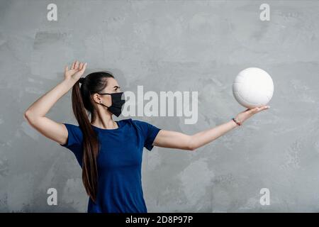 Young woman protective face mask with volleyball ball isolated on grey background. Protective masks against virus infection. Vintage color filter Stock Photo