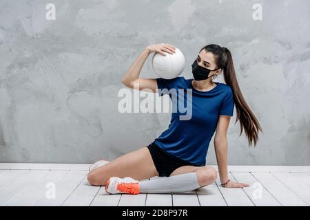 Young woman protective face mask with volleyball ball isolated on grey background. Protective masks against virus infection. Vintage color filter Stock Photo