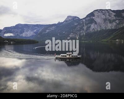 A boat on the calm Lake Hallstatt with mountains in background approaching the famous tourist village of Hallstatt Stock Photo