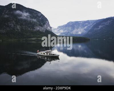 A boat on the calm Lake Hallstatt with mountains in background approaching the famous tourist village of Hallstatt Stock Photo