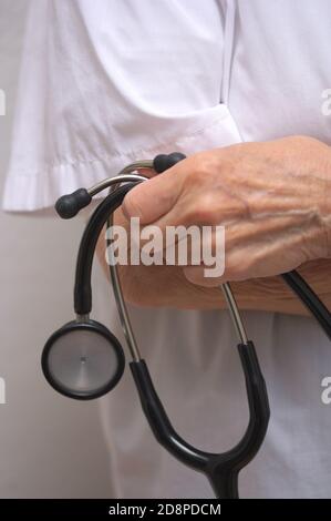 Close-up of a senior person holding a stethoscope in his hand with his arms crossed and wearing a white shirt Stock Photo