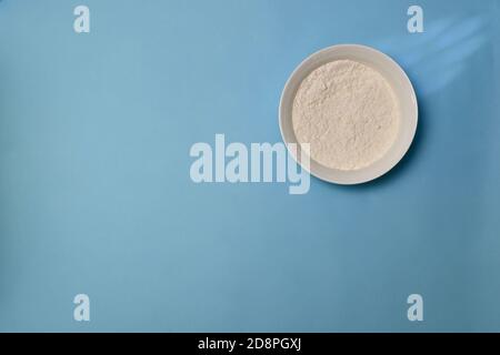 Wheat flour in a white deep plate, on the right, against a blue background. Stock Photo