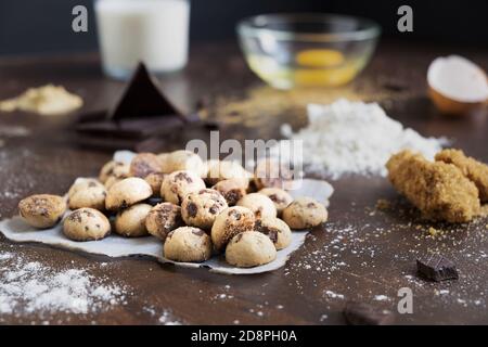 Shot of mini cookies on parchment paper with chocolate bars, flour, eggs, and milk on a table Stock Photo